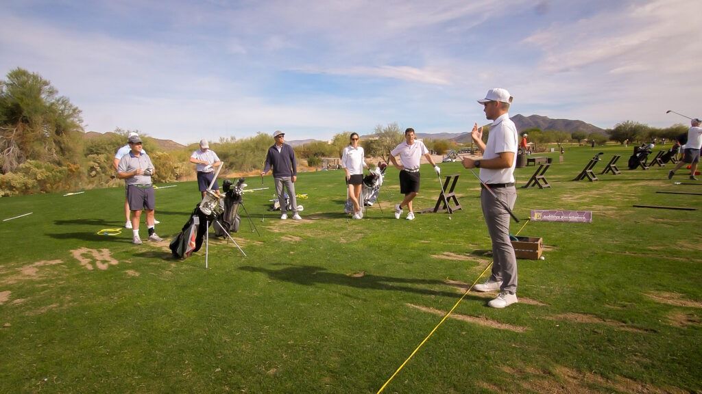 Modern golfers practicing swings and putting on a driving range during a professional golf school training session.